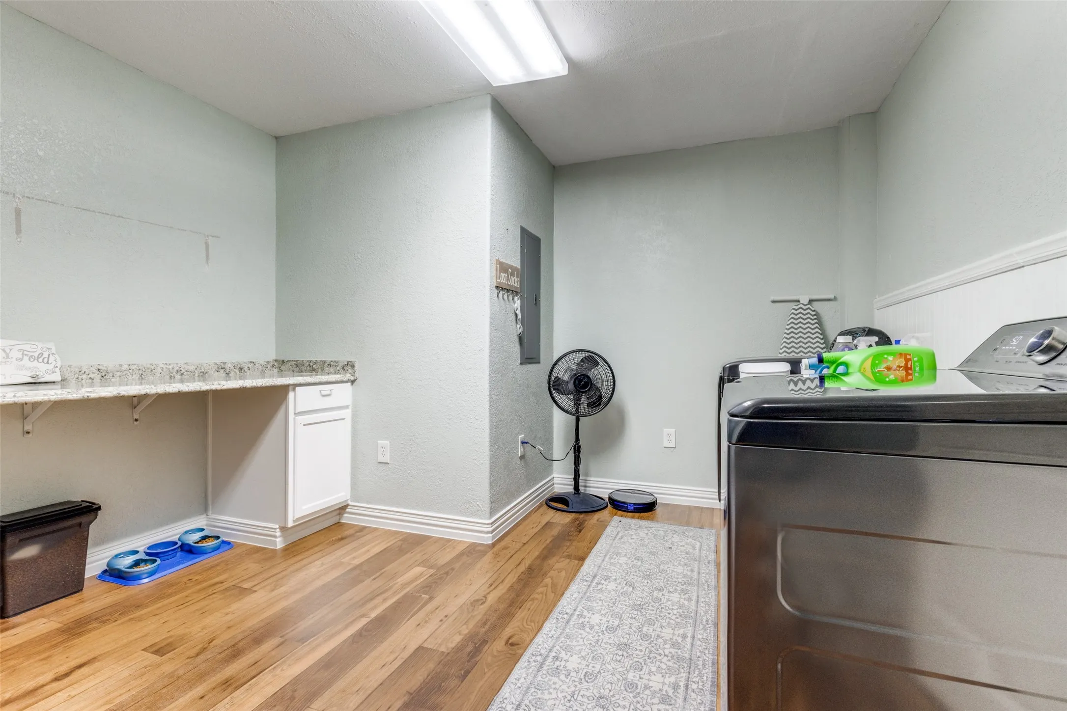 Laundry area featuring light wood-style flooring, a textured wall, an office area, electric panel, and washing machine and clothes dryer