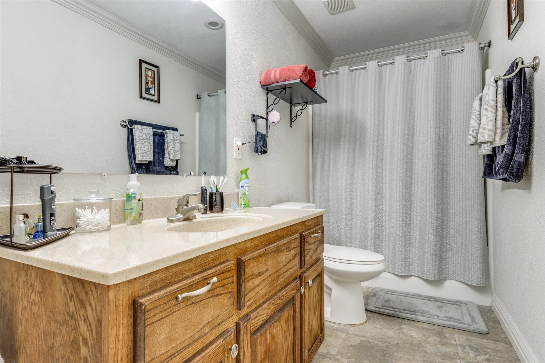 Bathroom with vanity, crown molding, shower / bathtub combination with curtain, and a textured wall