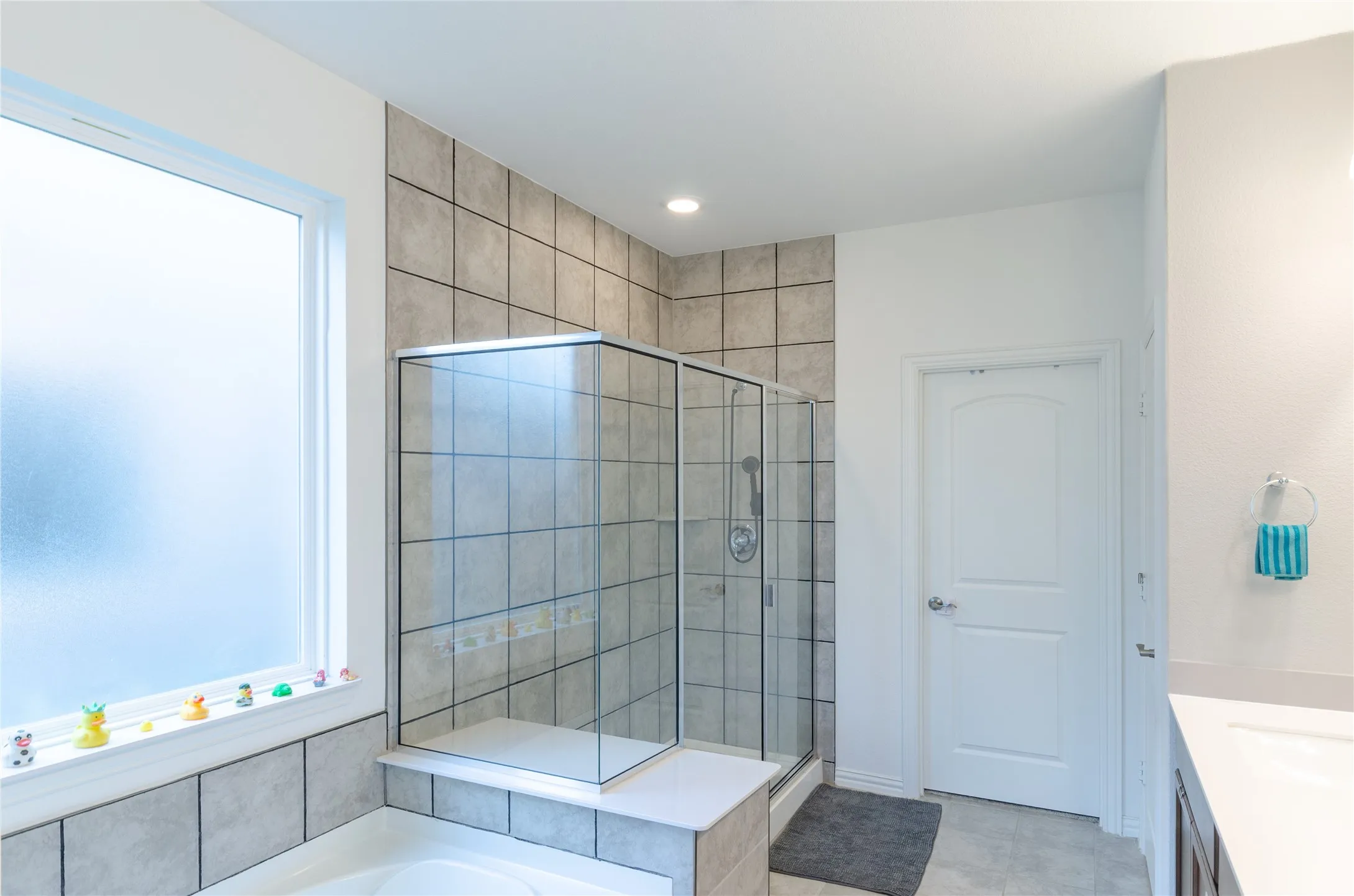 Glass-enclosed shower with tile surround, frosted privacy window, recessed lighting, and a built-in tub