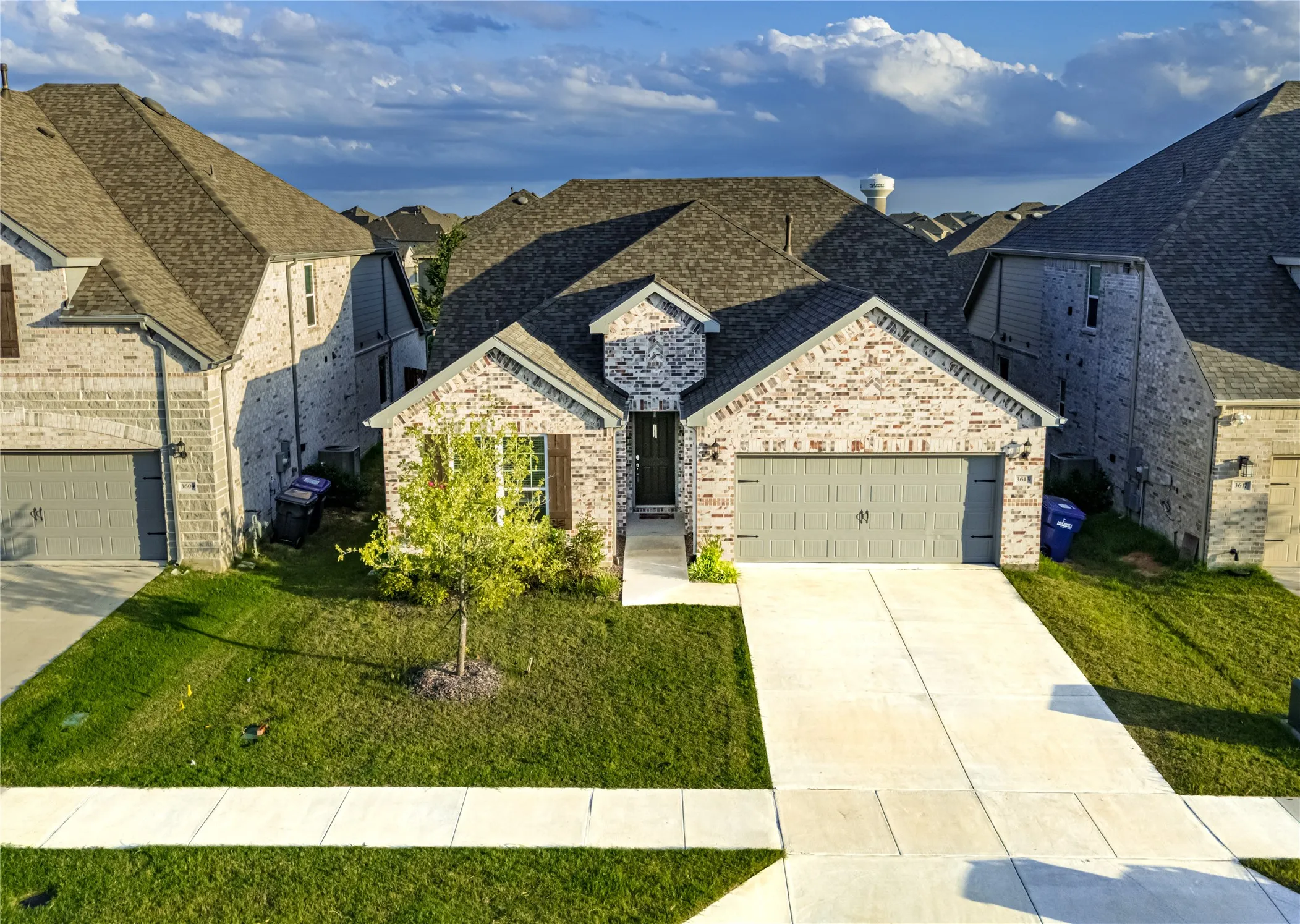 Brick facade residence featuring an attached two-car garage, concrete driveway, and a front yard with mature landscaping