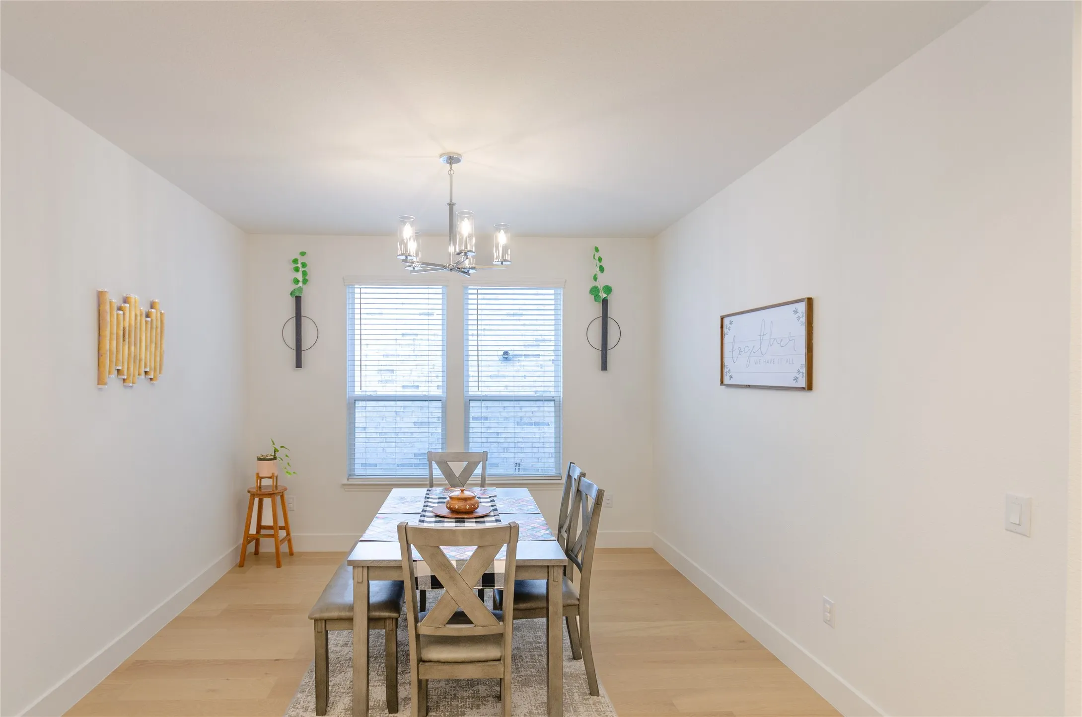 Dining area featuring a contemporary chandelier, two windows with blinds, light wood-finish flooring, and white baseboards