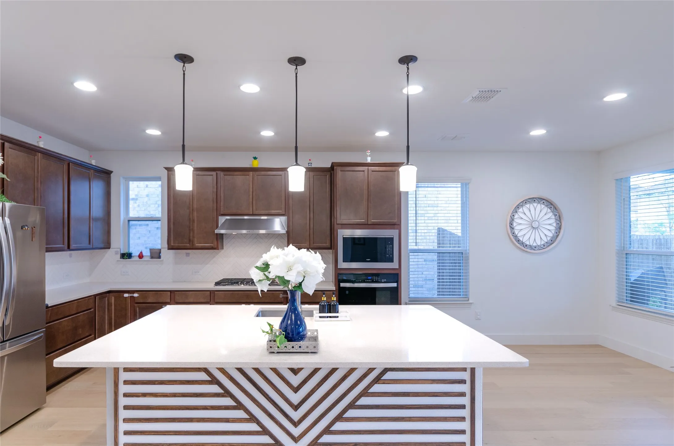 Spacious kitchen featuring an oversized island with decorative paneling, stainless steel appliances, dark wood cabinetry, and recessed lighting