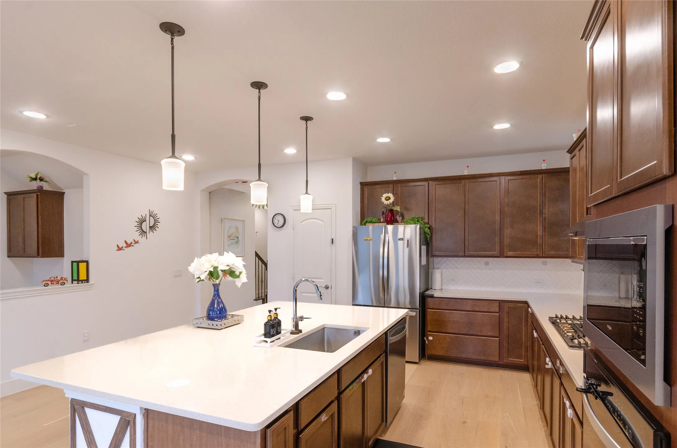 Modern kitchen featuring an expansive island with a stainless steel sink, under-cabinet storage, wood-finish flooring, and recessed lighting