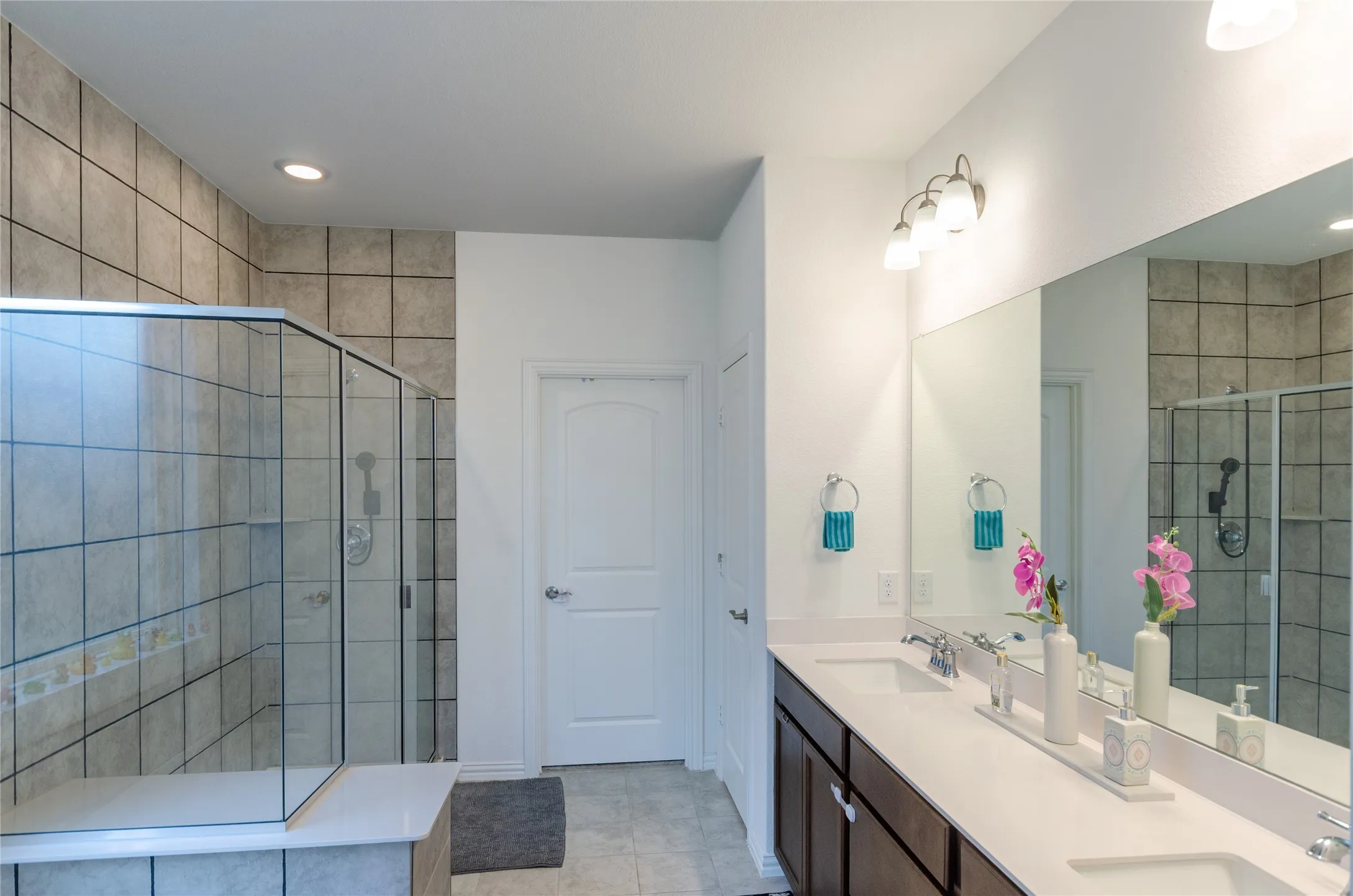 Spacious bathroom featuring a glass-enclosed shower with tile surround, dual vanity with undermount sinks, and broad wall mirror