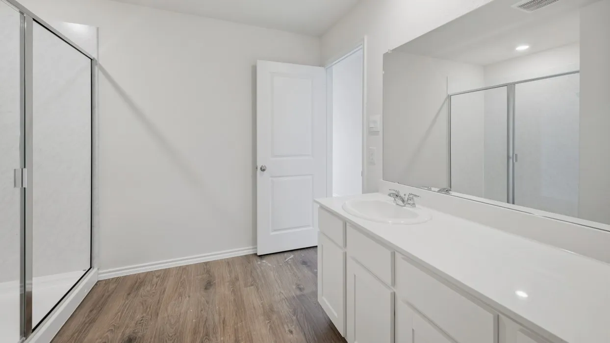Bathroom featuring a single-sink vanity with white cabinetry and a white countertop, a large vanity mirror, and a walk-in shower with a glass enclosure