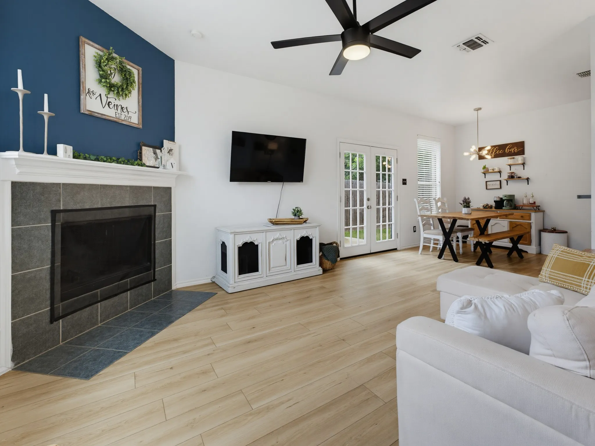 Living area featuring wood-finish flooring, a fireplace with a tiled surround, white mantel, and a contrasting blue accent wall