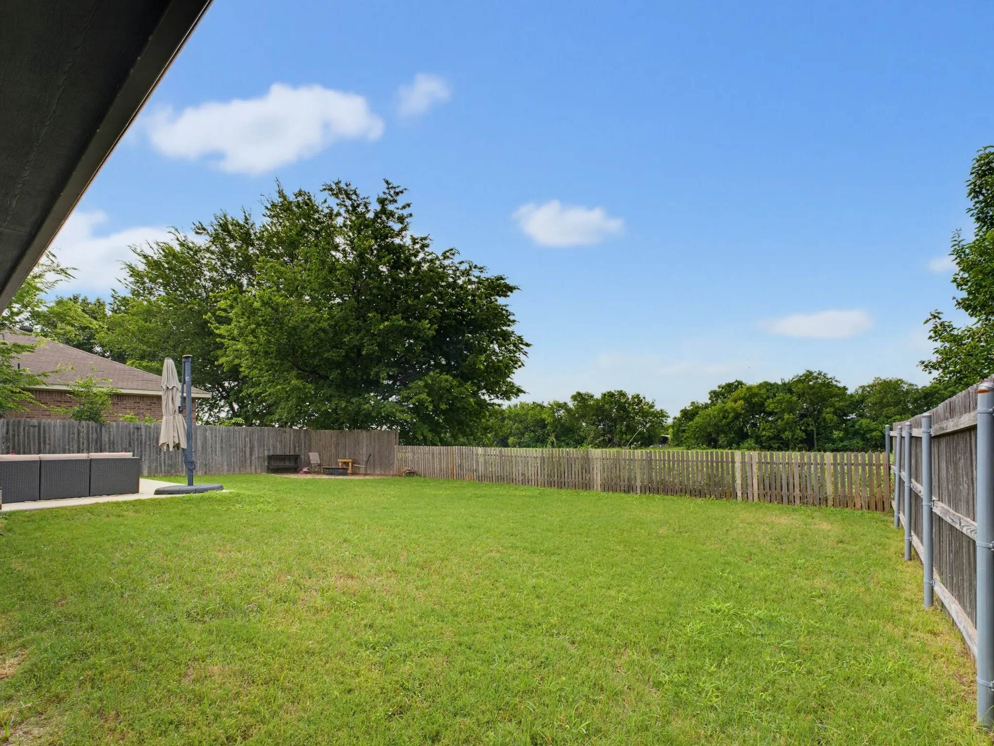 Expansive rear yard featuring a large grass area, a concrete patio, and mature perimeter trees