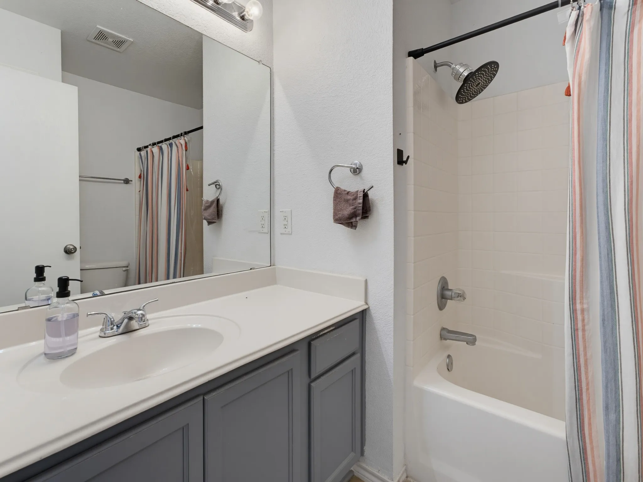 Bathroom featuring a single vanity with a light-toned countertop, gray shaker-style cabinetry, an integrated sink basin, a chrome faucet, and a large wall-mounted mirror