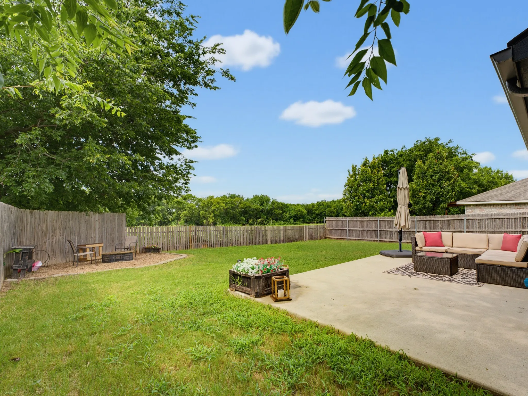 Expansive backyard featuring a concrete patio, wood privacy fencing, and lush green lawn