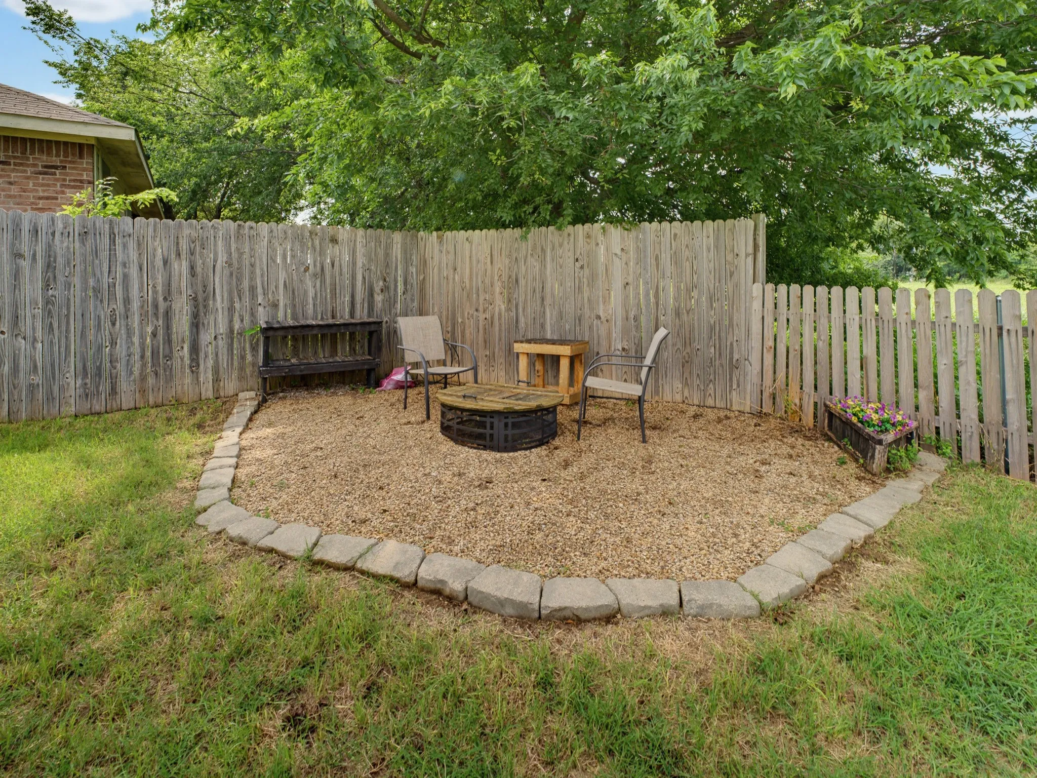 Landscaped gravel patio area bordered by stone pavers and surrounded by a wood privacy fence