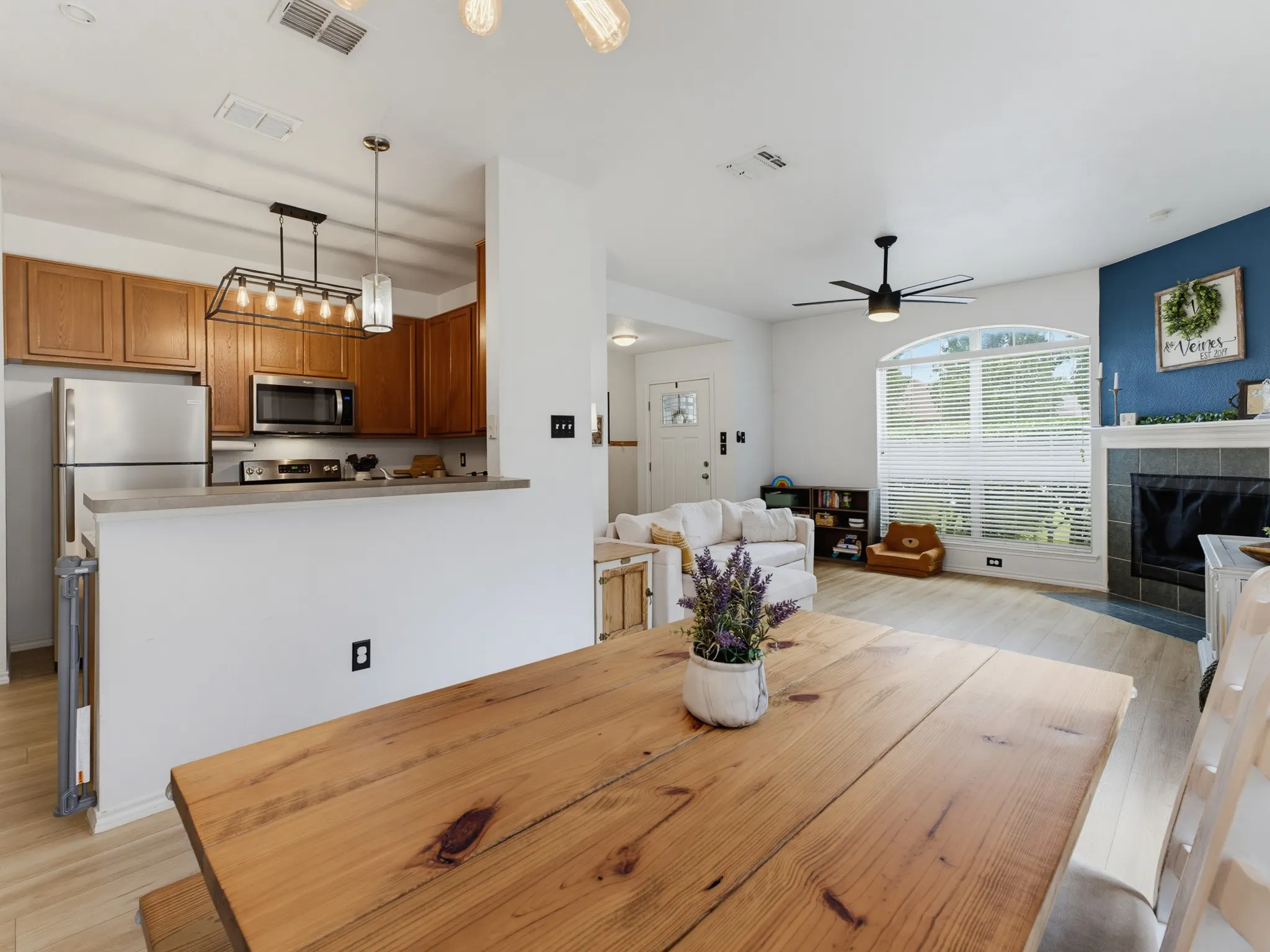 Open-concept living space featuring wood-finish flooring, a kitchen with stainless steel appliances, a breakfast bar, a fireplace with a mantel, and an arched window