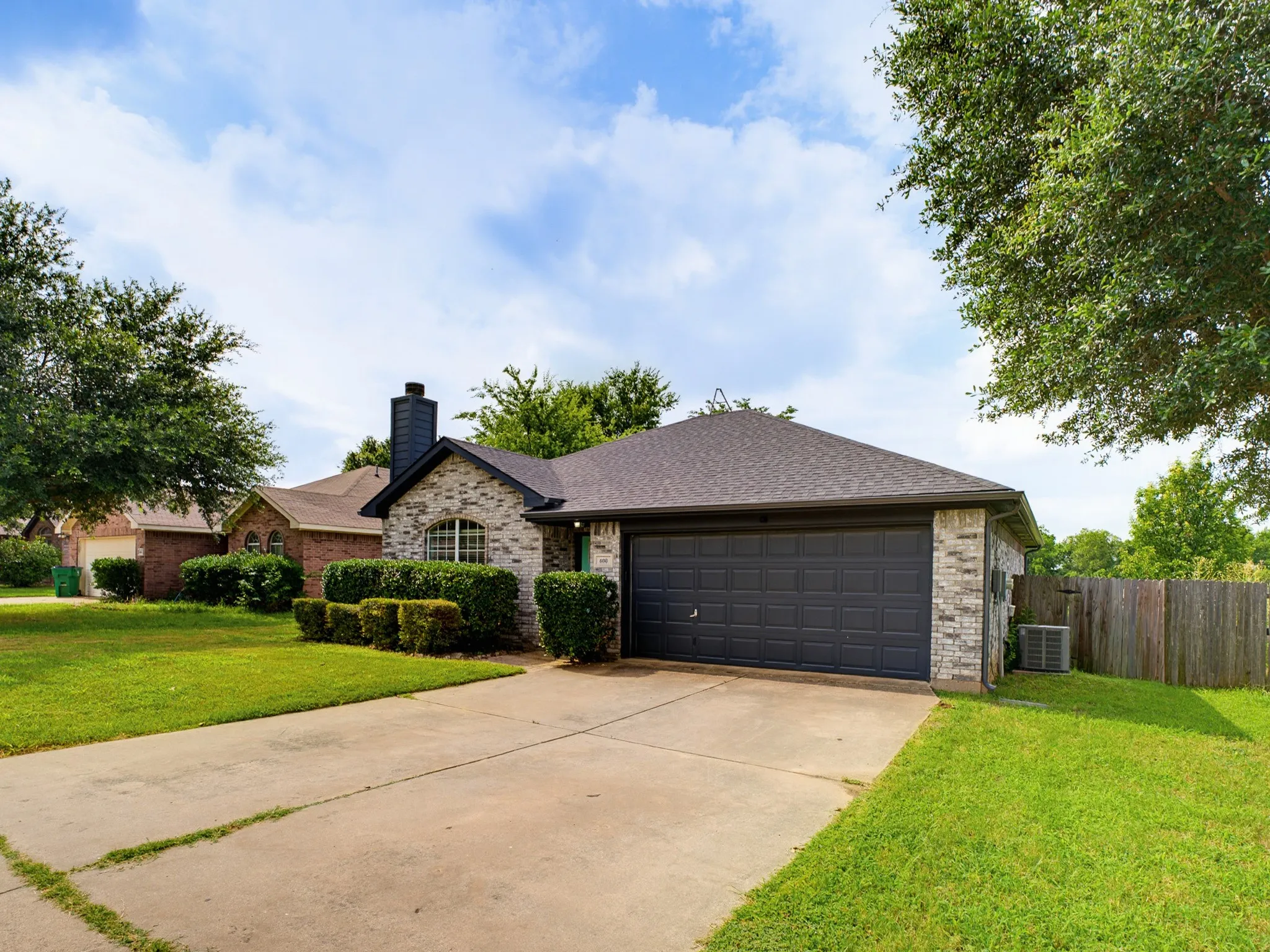 Brick exterior featuring a dark gray garage door, a dark shingle roof, and a prominent black chimney