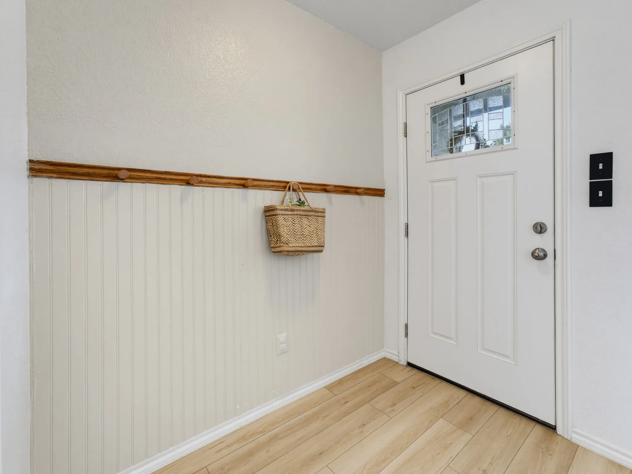 Entryway featuring a white paneled door with decorative glass, wood-finish flooring, and white beadboard paneling with a wood trim detail