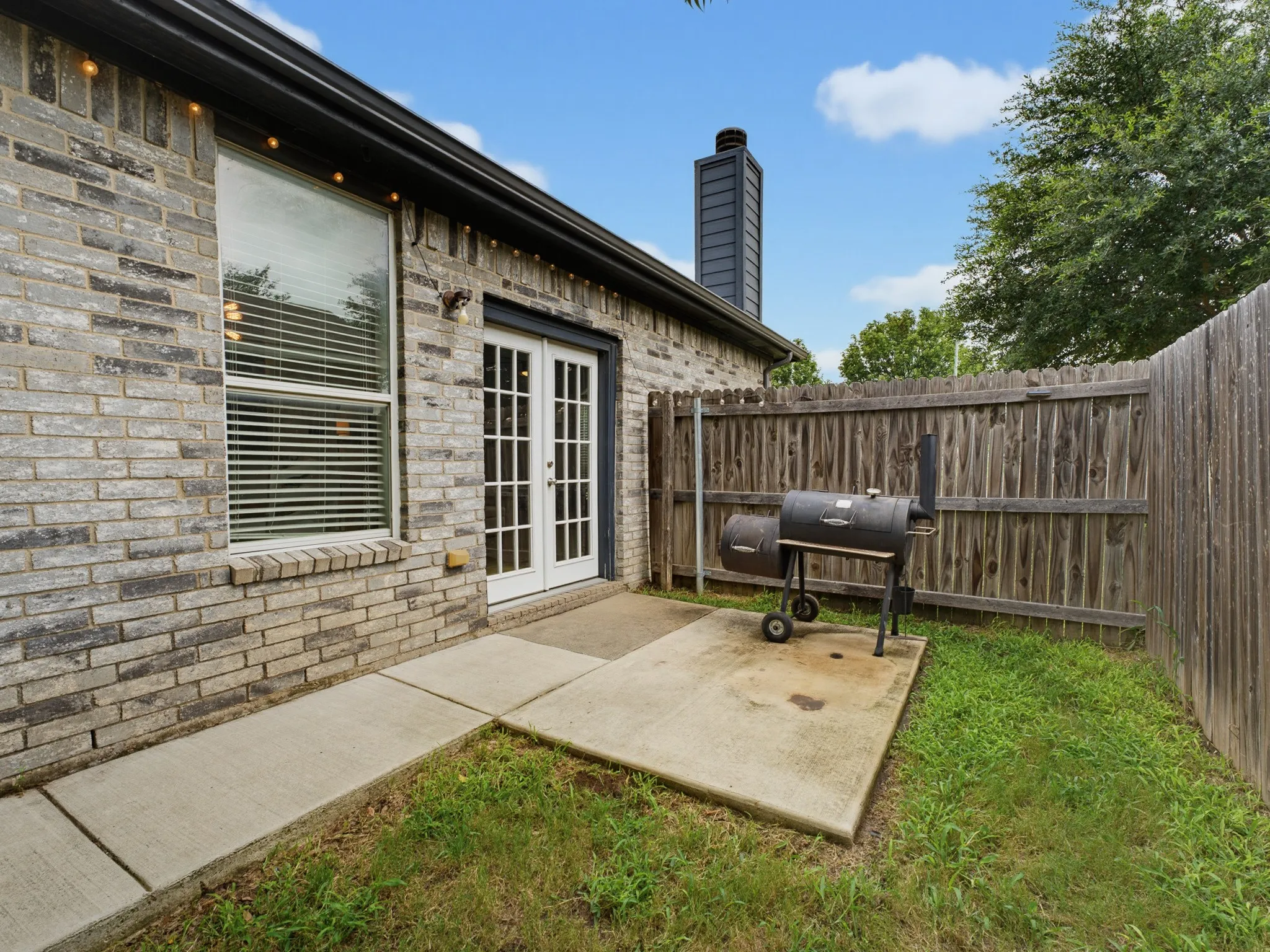 Brick exterior featuring a patio area with a concrete slab, wood privacy fencing, and a modern black chimney