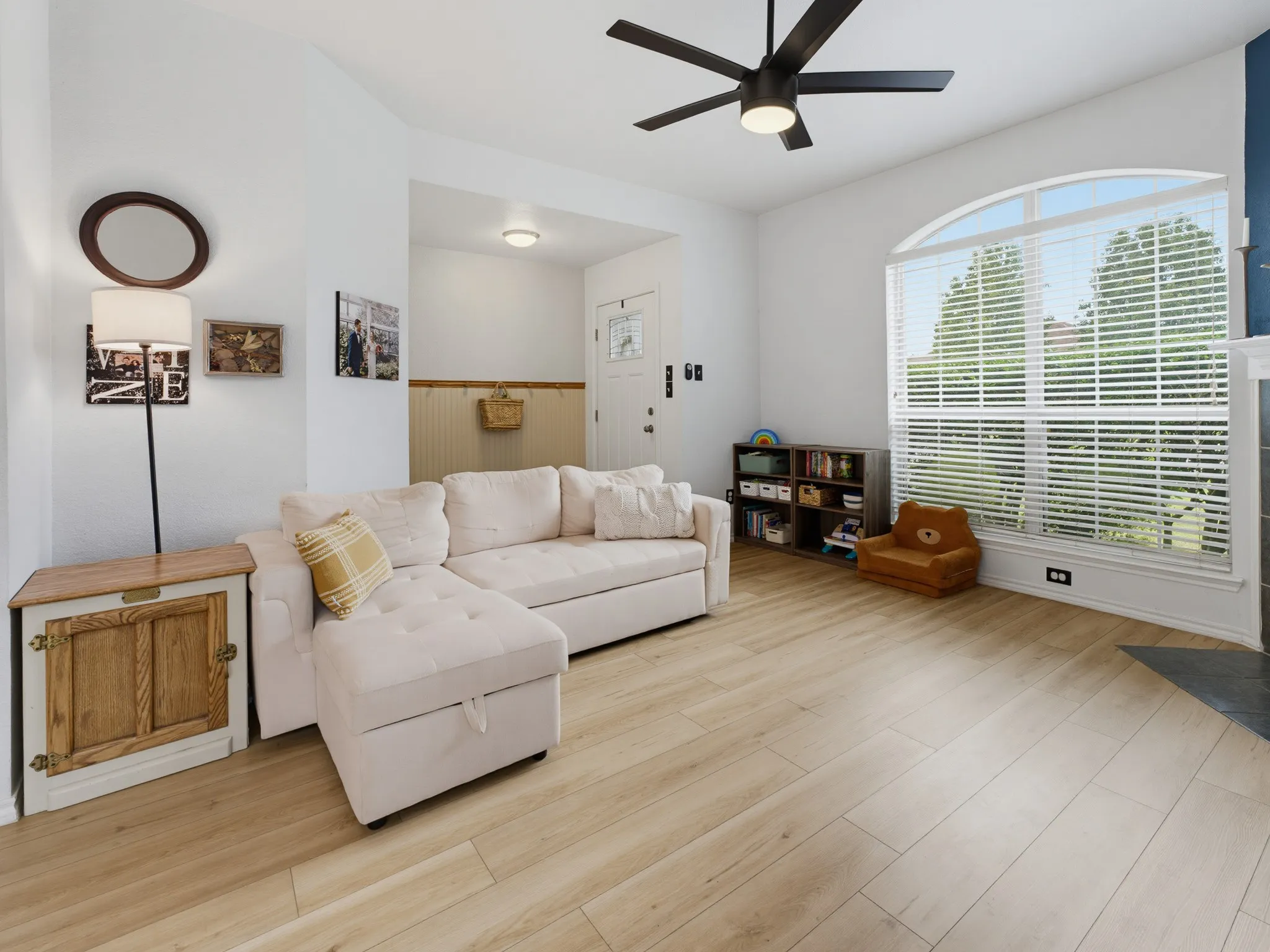 Spacious living area featuring light wood-finish flooring, a contemporary ceiling fan, and an arched window with blinds