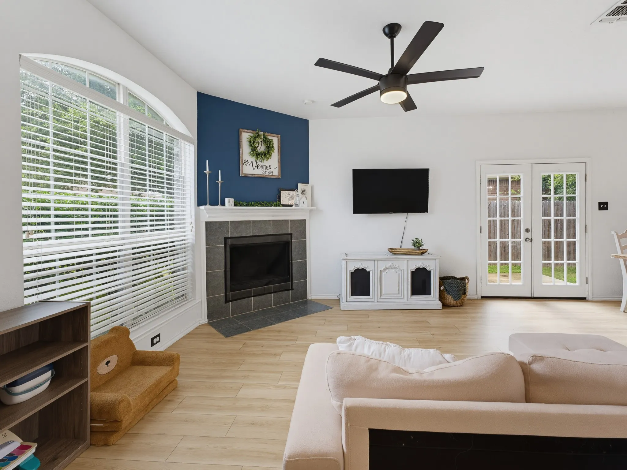 Spacious living area featuring light wood-finish flooring, a contemporary ceiling fan, and an arched window with blinds