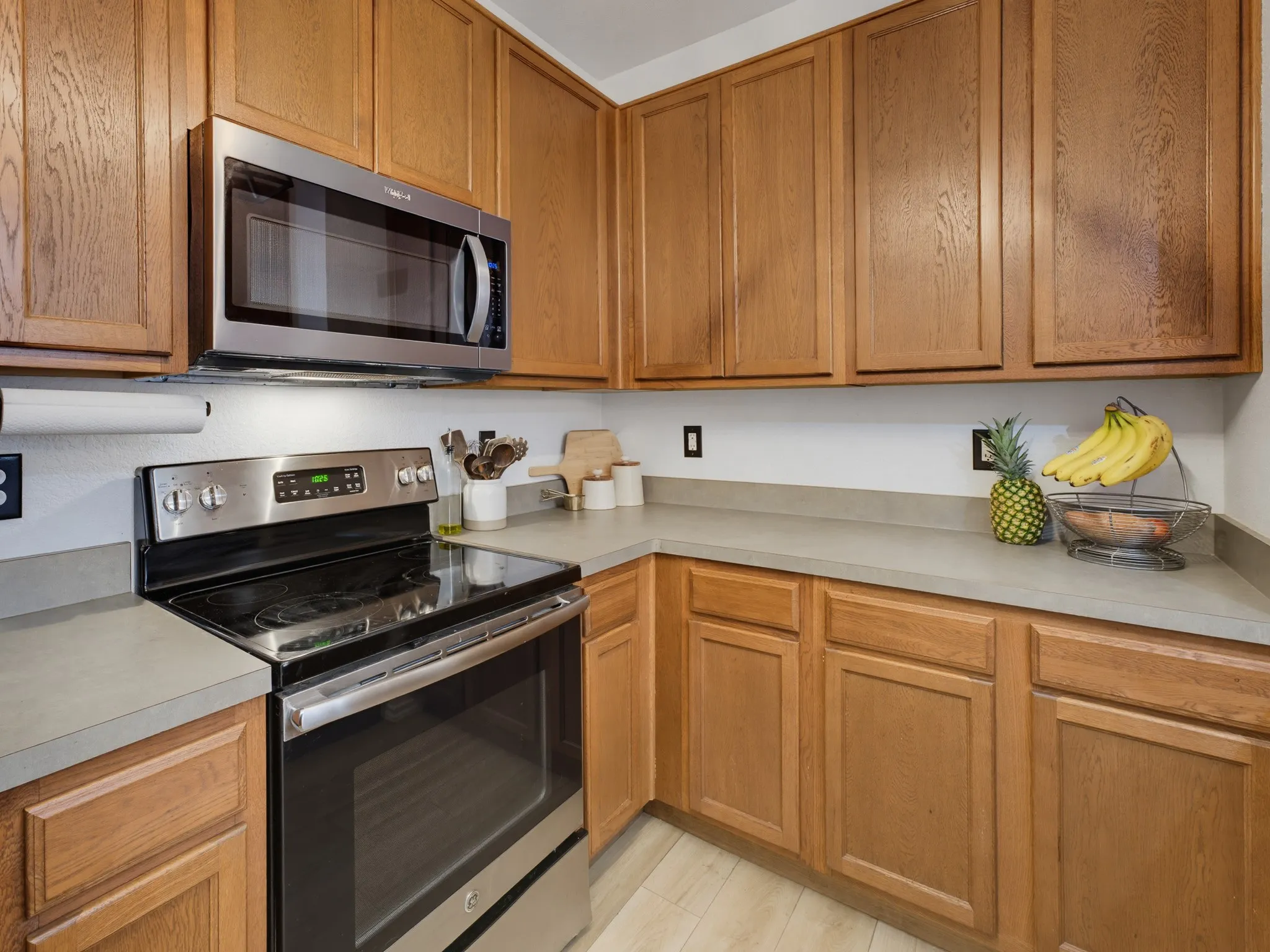 Kitchen featuring wood cabinetry, stainless steel range and microwave, light-toned countertops, and wood-finish flooring