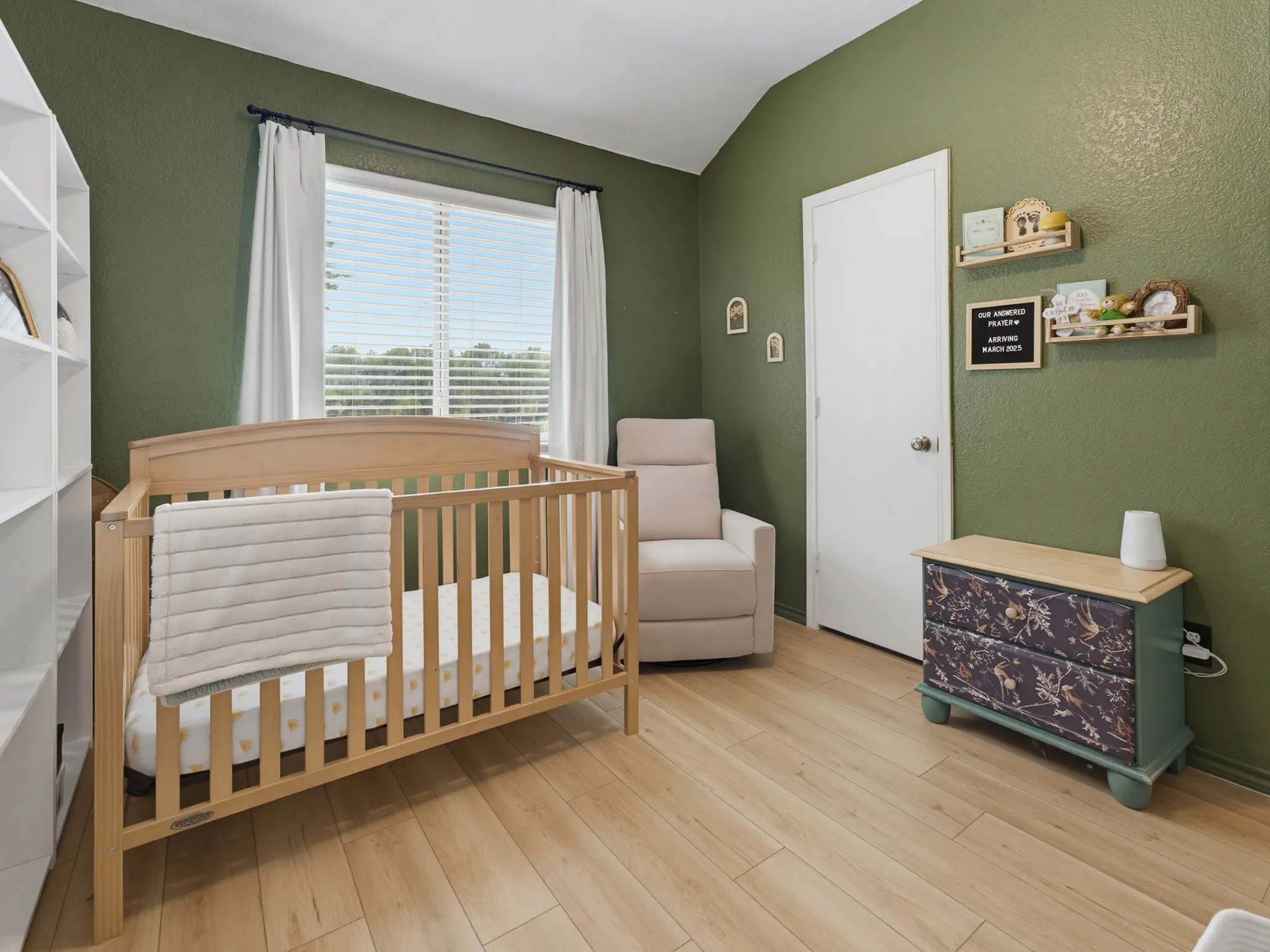 Room featuring a vaulted ceiling, wood-finish flooring, and a large window with blinds and white curtains