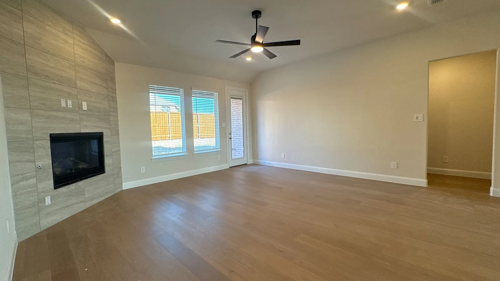 Wood-finish flooring, tiled fireplace surround, recessed lighting, ceiling fan, and large windows