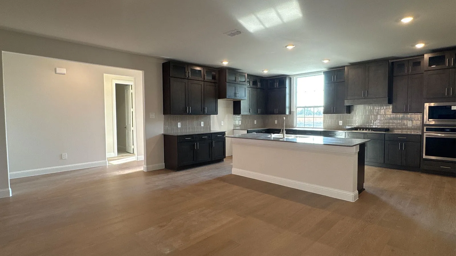 Open-concept kitchen with dark wood-finish cabinetry, stainless steel appliances, a large center island, and wood-finish flooring