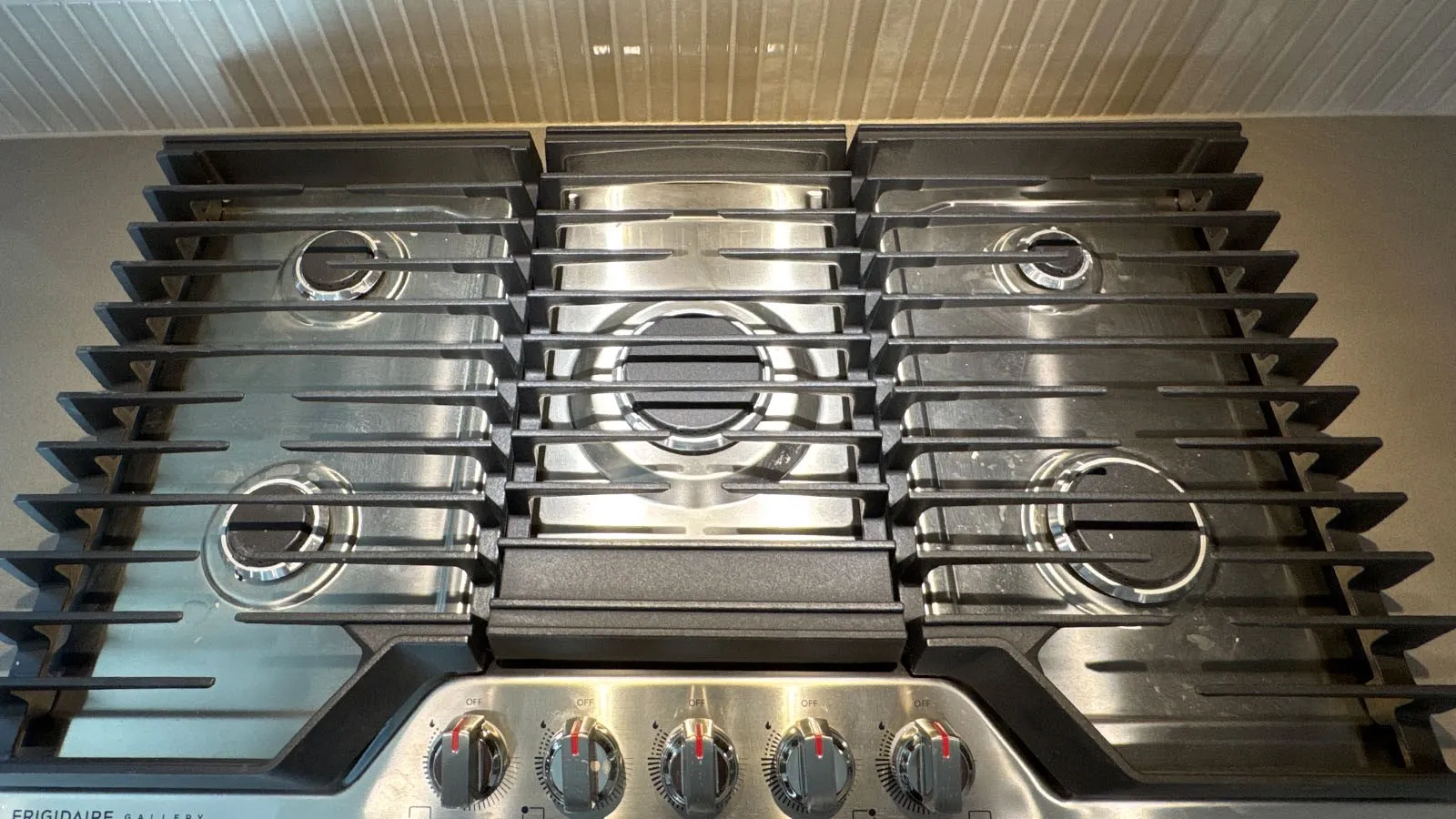 Stainless steel cooktop with five burners, cast iron grates, and control knobs