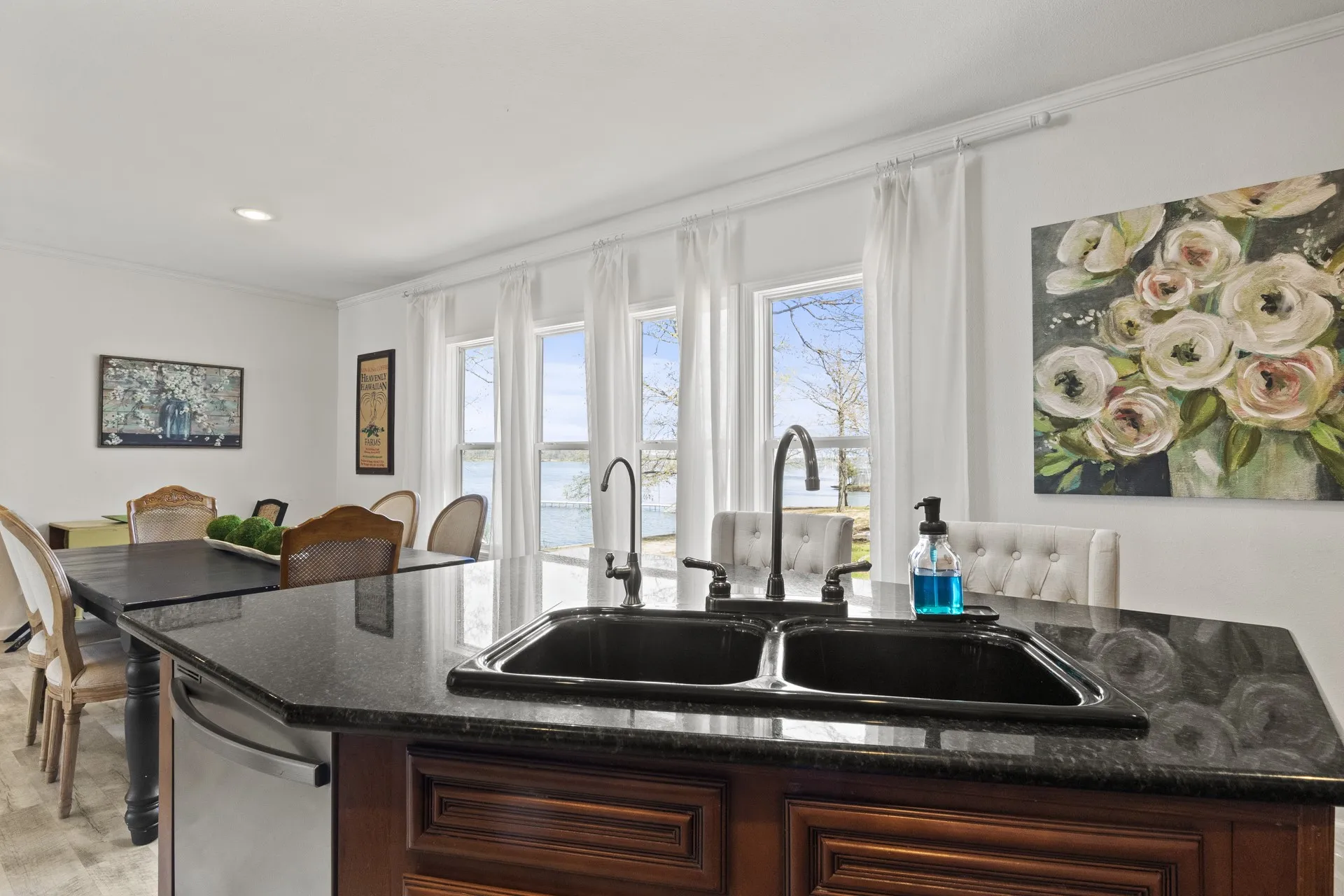 Kitchen with dark stone countertops, sink, light colored carpet, dishwasher, and an island with sink