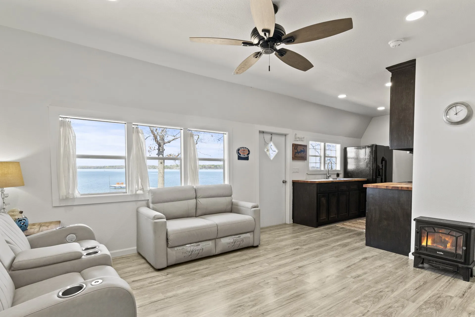 Living room featuring ceiling fan, a water view, sink, light wood-type flooring, and a wood stove