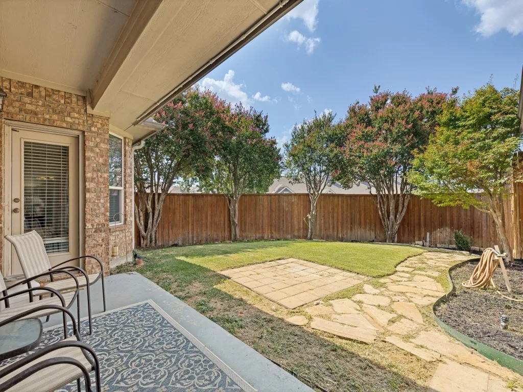Covered patio with brick exterior, leading to a landscaped backyard featuring a flagstone pathway, a privacy fence, and mature trees