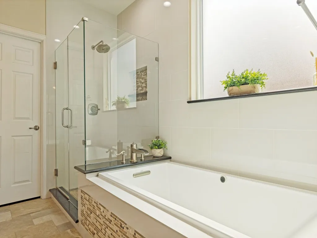 Modern bathroom featuring a frameless glass shower enclosure, a built-in soaking tub with a dark countertop surround, and an integrated shower head