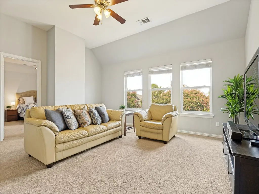 Carpeted living area featuring a vaulted ceiling with a ceiling fan, three horizontal windows, and light gray walls