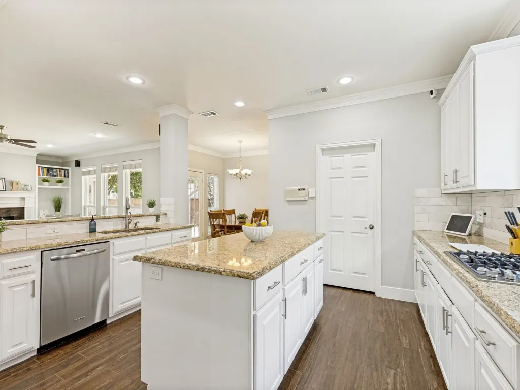 Kitchen featuring a central island, granite countertops, white cabinetry, stainless steel dishwasher, and wood-finish flooring