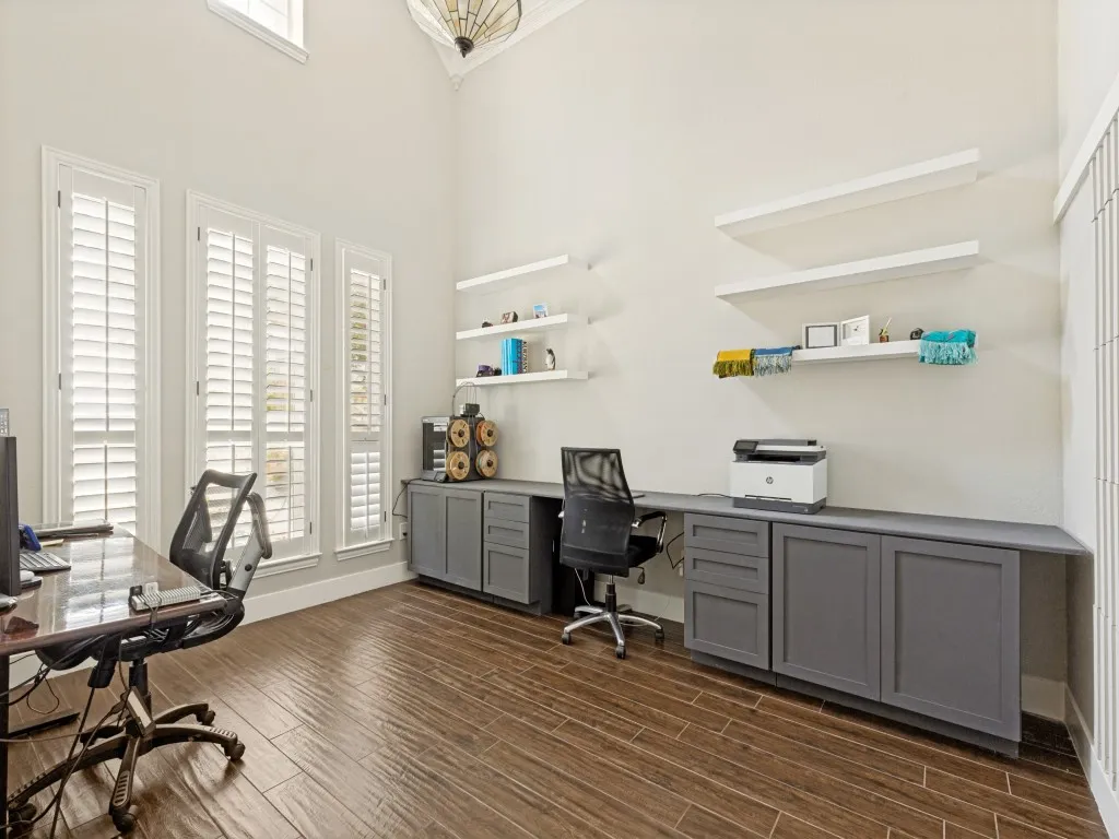 Dedicated workspace featuring wood-finish flooring, high ceilings with a decorative light fixture, and multiple windows with white plantation shutters
