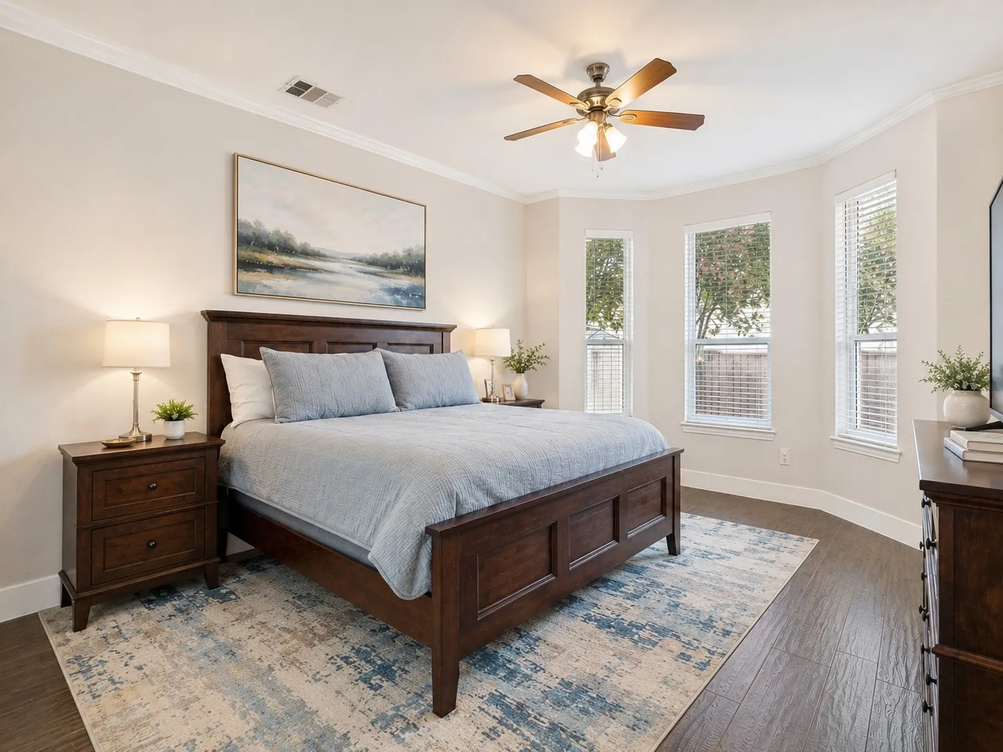 Bright bedroom featuring a bay window with three vertical windows, wood-finish flooring, crown molding, and a ceiling fan