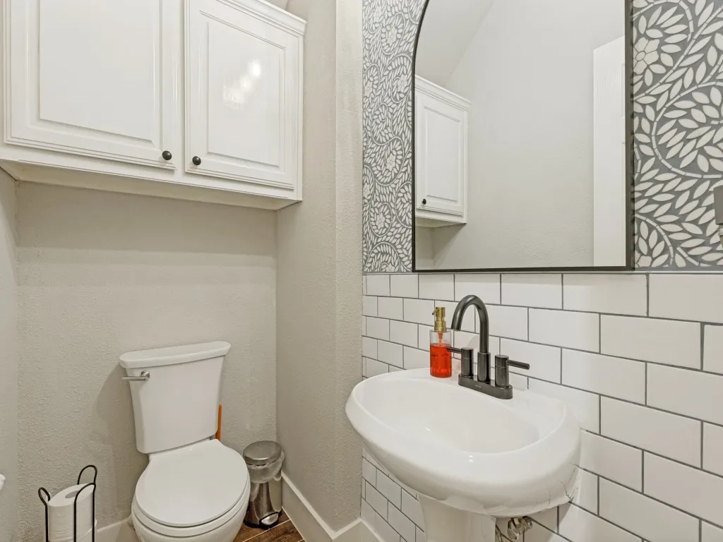 Powder room featuring a pedestal sink with matte black faucet, subway tile wainscoting, an arched mirror, and decorative wallpaper accents