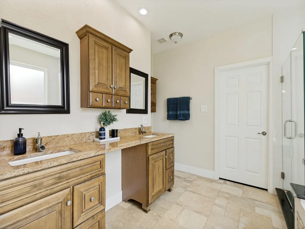 Double vanity with granite countertops, wood-finish cabinetry, and framed mirrors