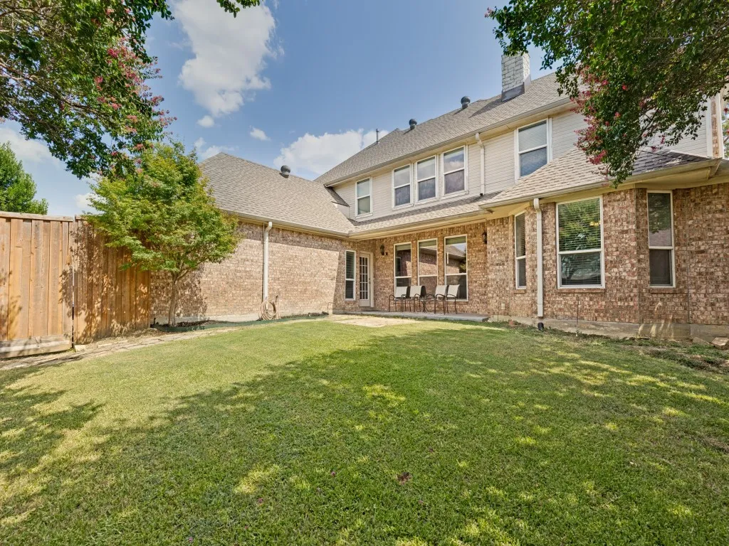Spacious backyard featuring a manicured lawn, full-height privacy fencing, and a brick exterior with multiple windows