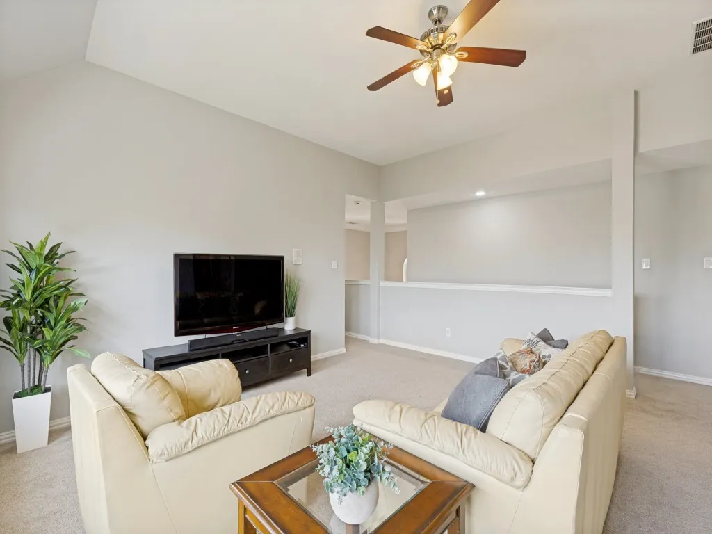 Living area featuring a vaulted ceiling, ceiling fan with integrated lighting, and carpeted flooring