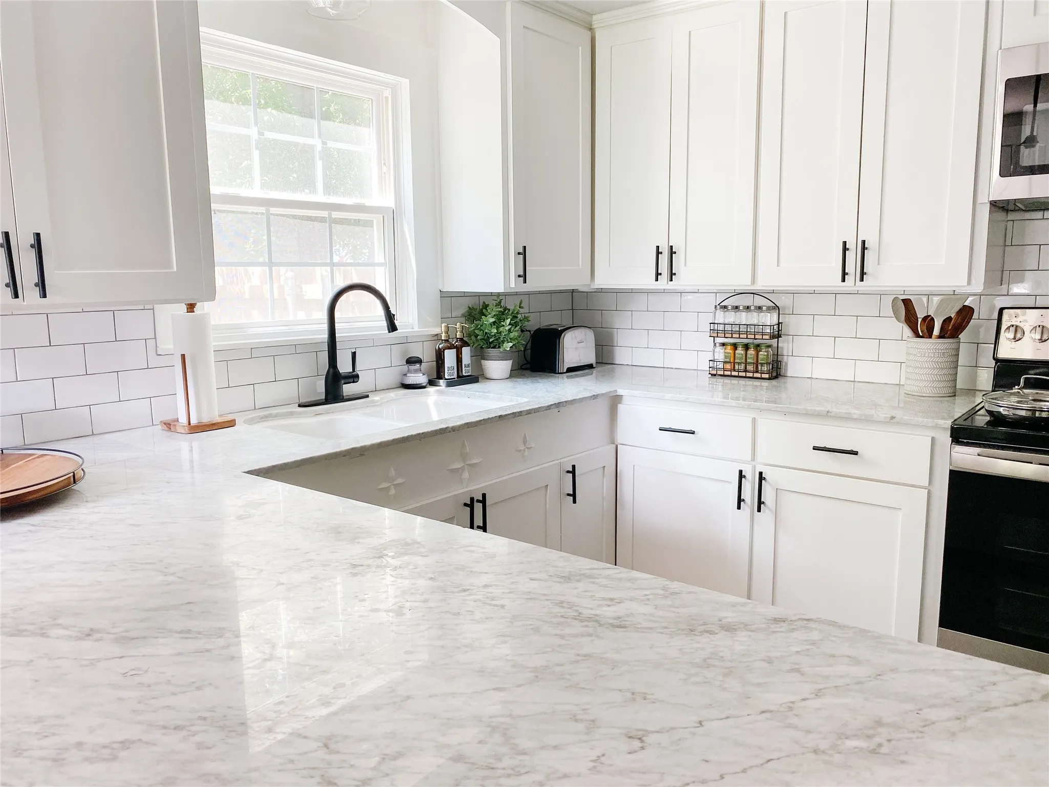 White kitchen featuring extensive counter space, subway tile backsplash, white shaker cabinetry, and an undermount double basin sink with a matte black gooseneck faucet