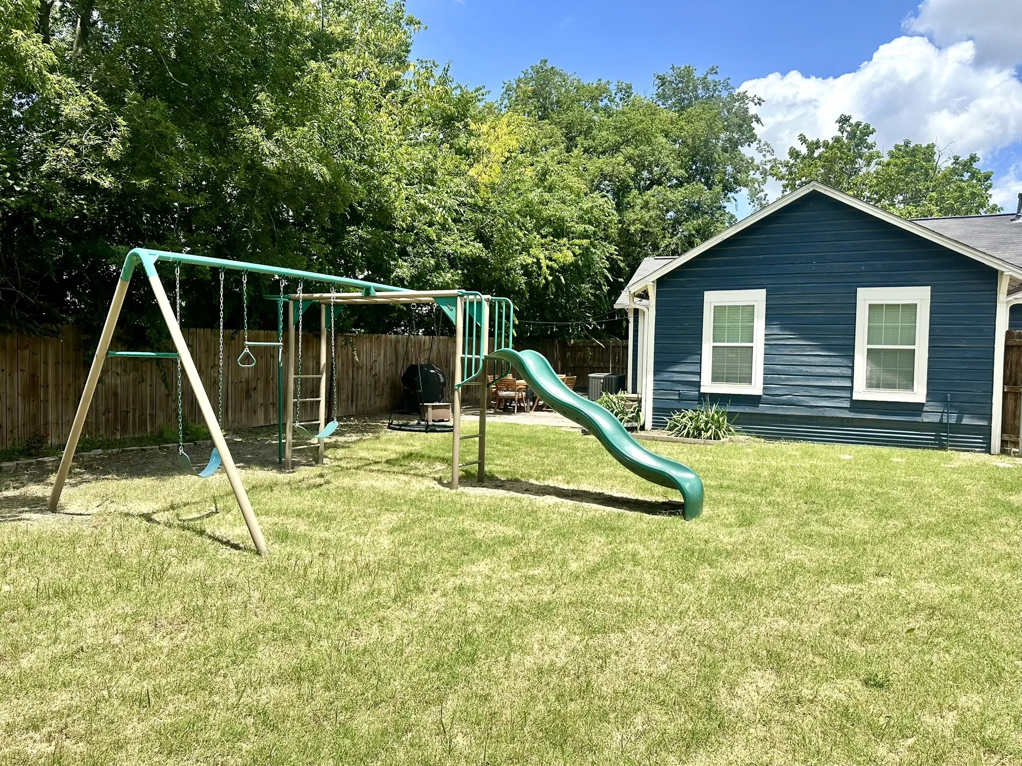 Expansive fenced backyard featuring a detached structure with blue siding, white trim windows, and established perimeter trees