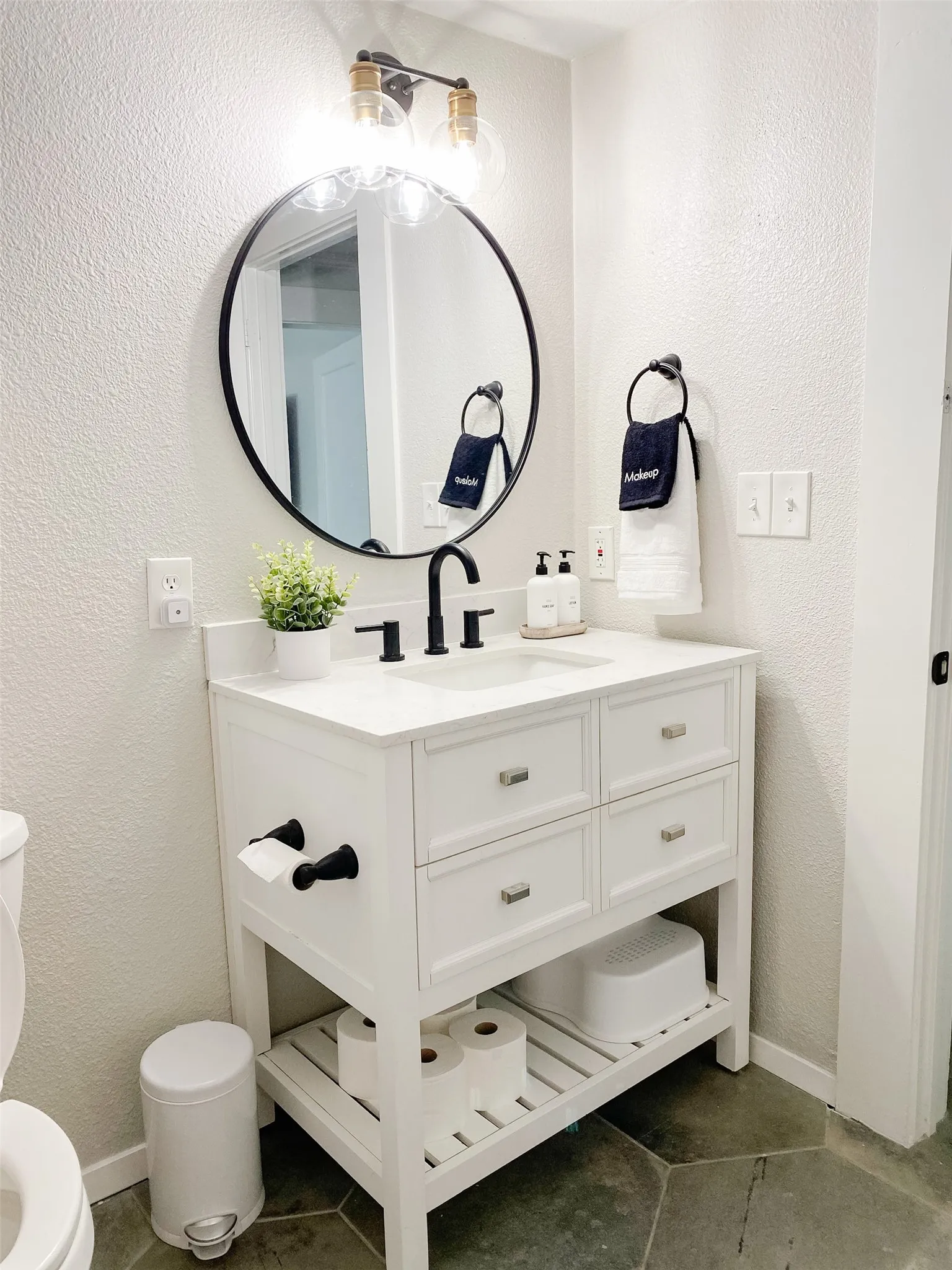 White vanity with integrated sink, black fixtures, and a round wall-mounted mirror