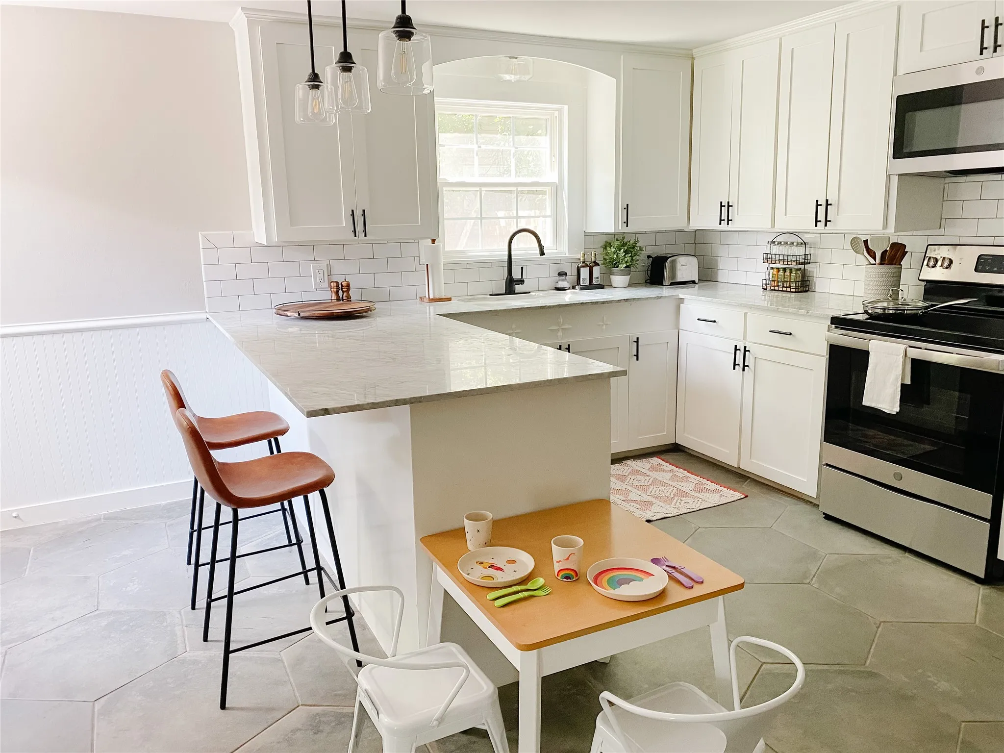 Kitchen featuring white shaker cabinetry with matte black hardware, light-toned countertops, white subway tile backsplash, and stainless steel appliances