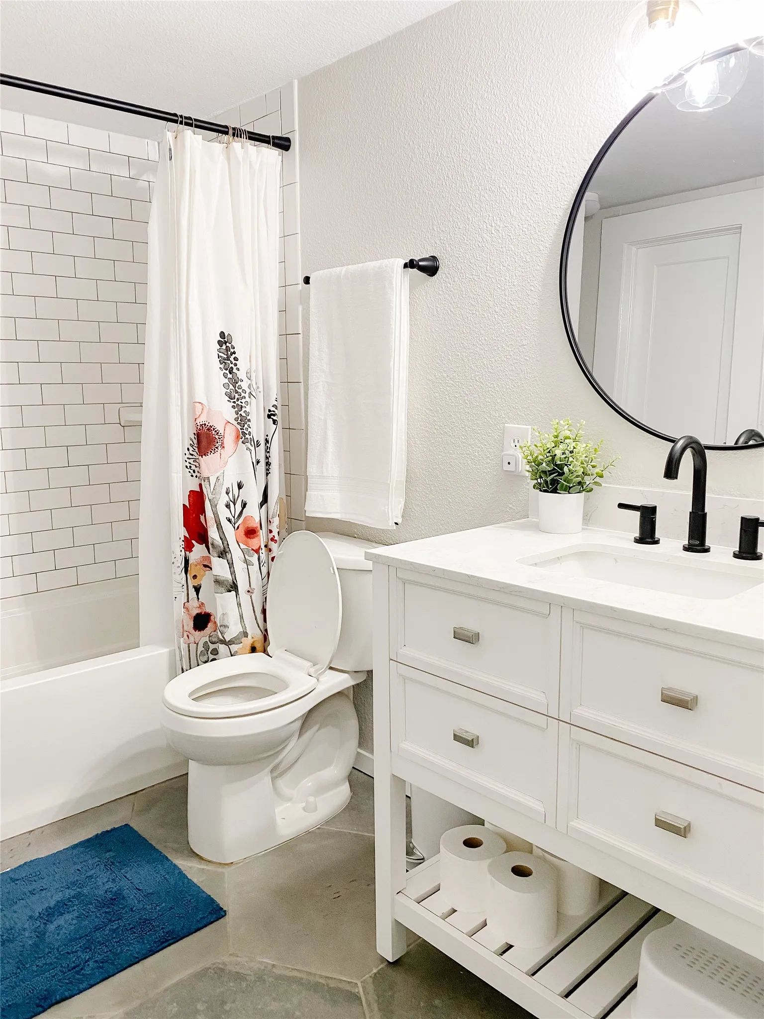 Bathroom featuring a white subway tile shower surround, a white vanity with brushed nickel hardware, and a black-framed round mirror