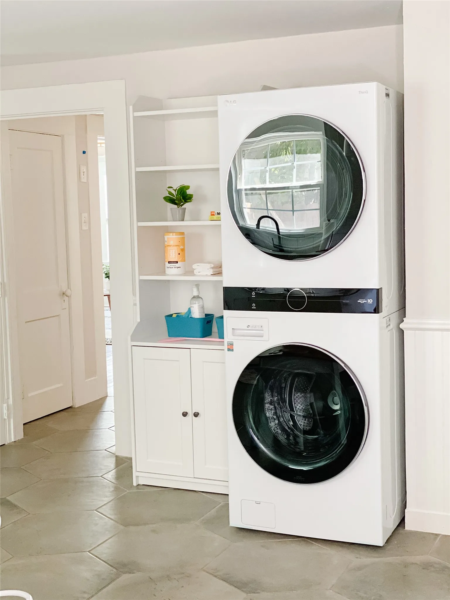 Laundry area featuring a stacked washer and dryer unit, white built-in shelving, white base cabinetry with doors, and hexagonal floor tiles