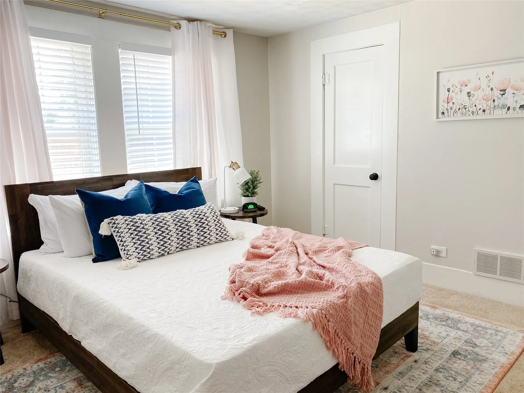 Hardwood-finish bed frame, dual windows with blinds and curtains, crisp white trim, and light-toned walls