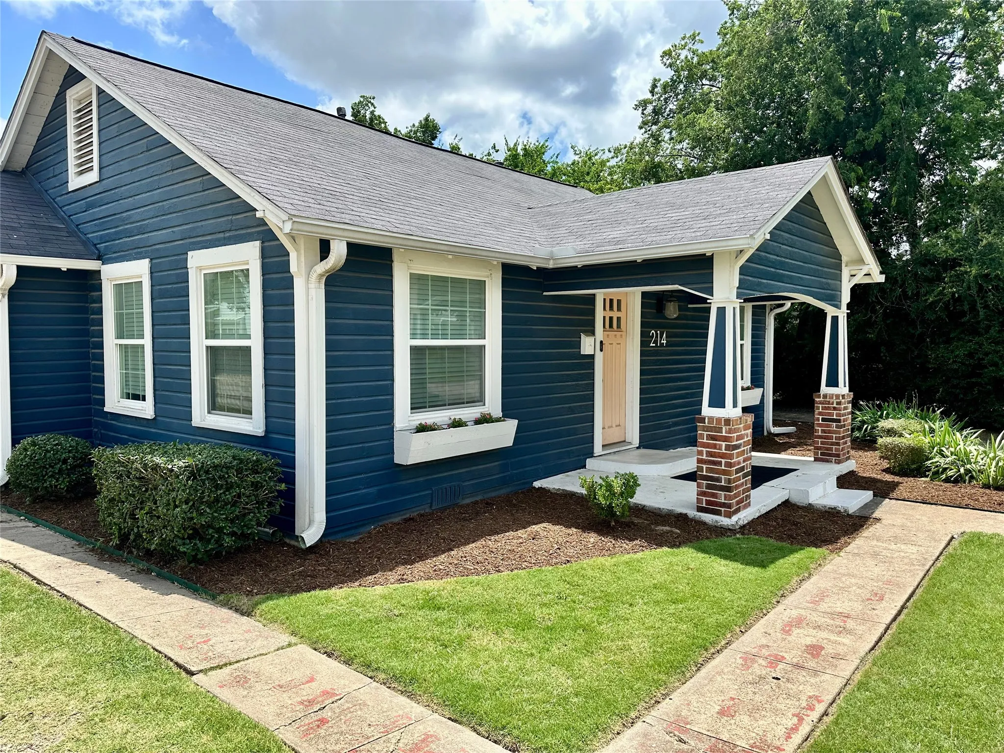 Exterior featuring blue horizontal siding, a light-colored front door, and a covered entryway with brick-wrapped columns