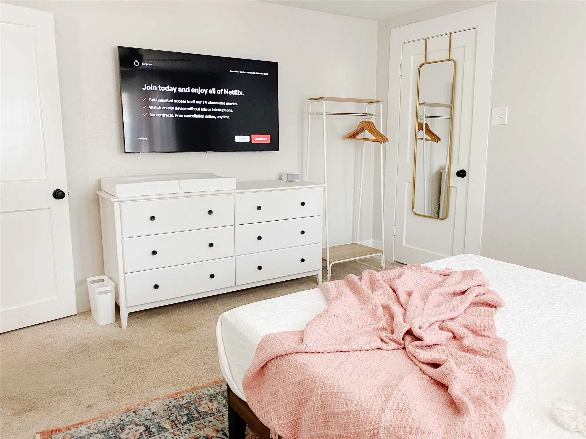Light-colored walls featuring a wall-mounted television and a white six-drawer dresser with black hardware
