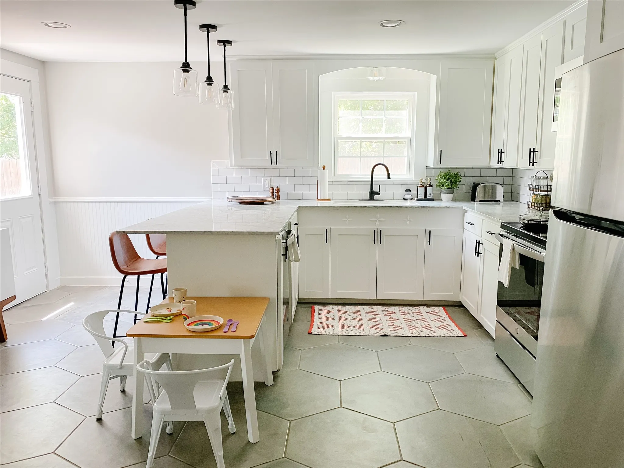 Kitchen featuring white shaker cabinetry, an integrated kitchen island with seating, hexagonal floor tiling, and a white subway tile backsplash