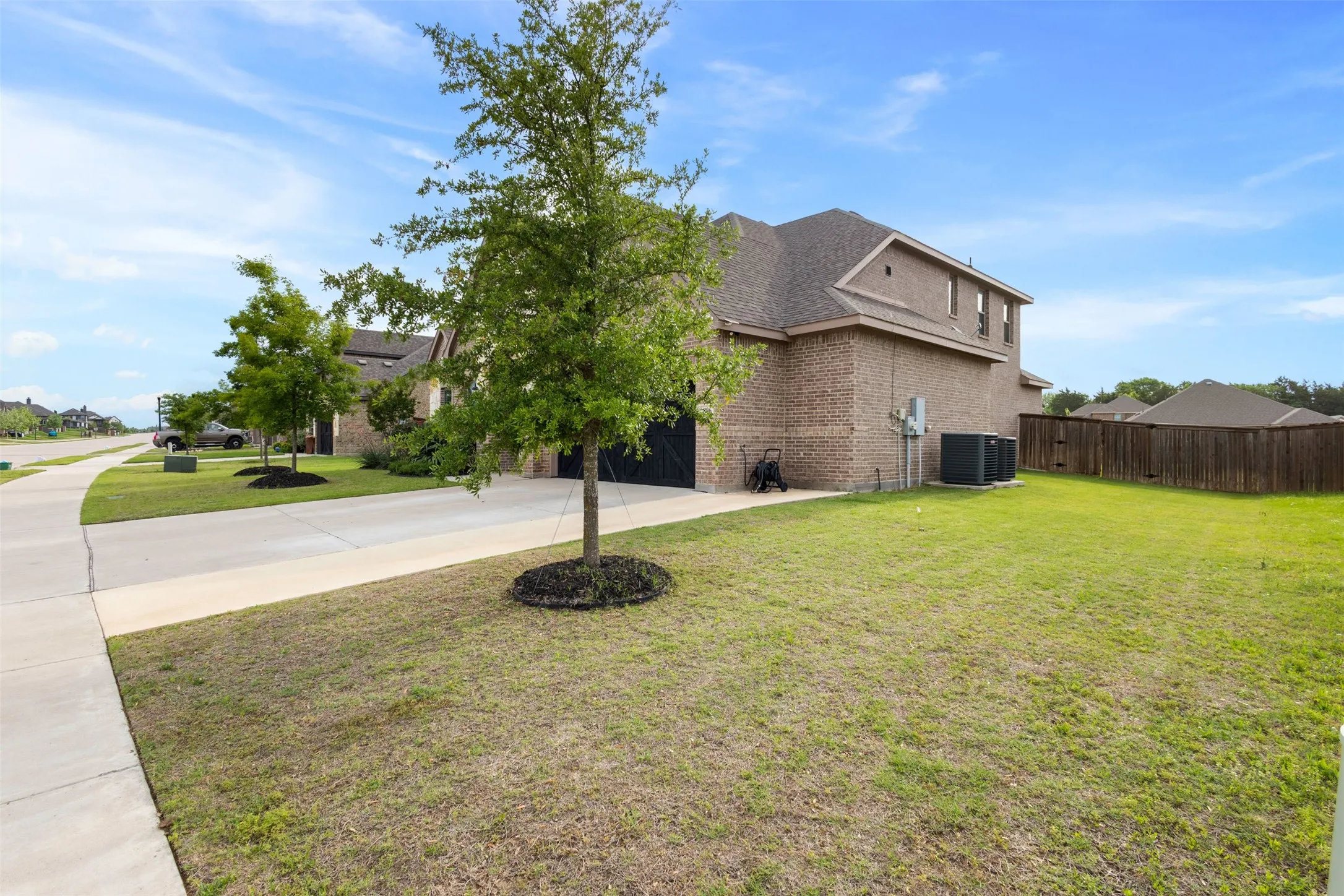 Brick exterior residence with a private backyard featuring a wood fence, mature trees, and a concrete driveway