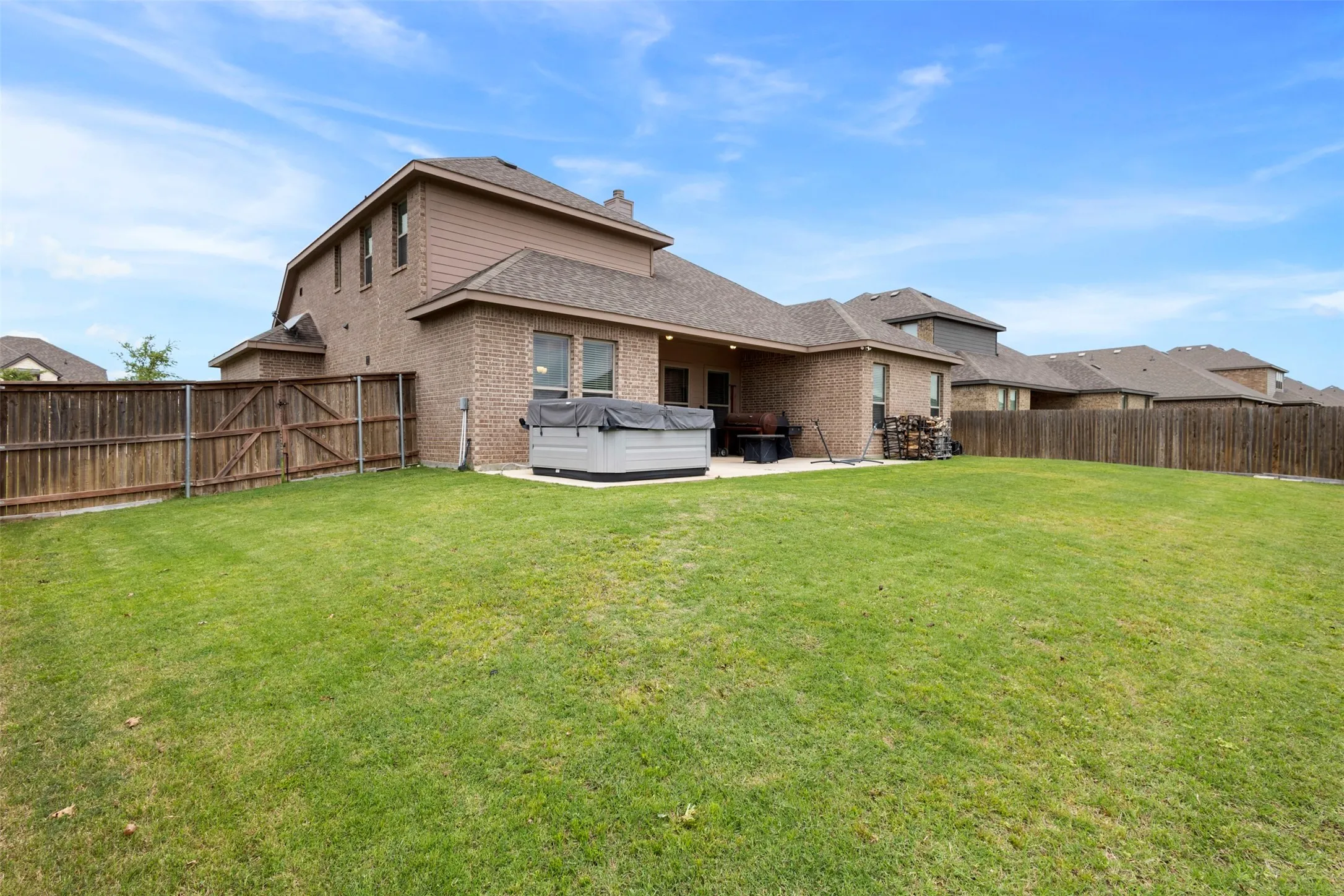 Expansive backyard featuring a manicured lawn, full privacy fencing, a concrete patio, and a two-story brick and siding exterior