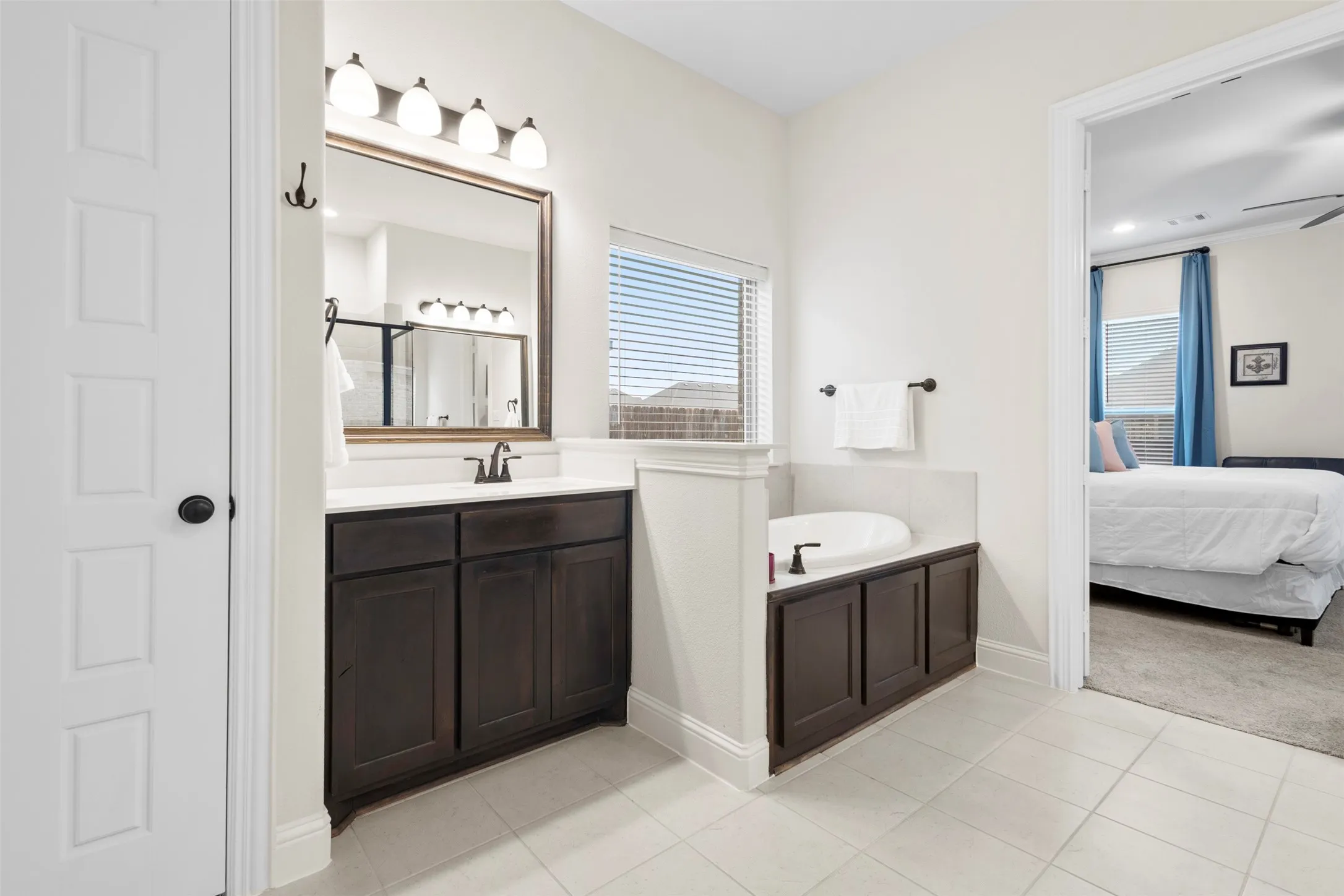 Bathroom featuring a built-in soaking tub, a single vanity with a white countertop and dark wood-finish cabinetry, a large framed mirror, and a wall-mounted light fixture
